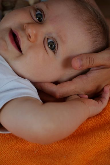 Ein lächelndes Baby liegt auf einer orangefarbenen Decke, mit einer Hand, die seinen Arm hält.