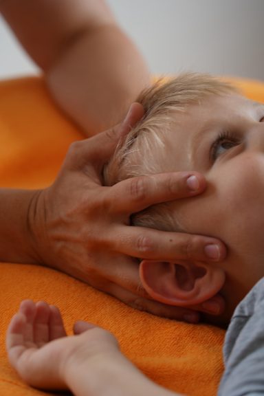 Eine Hand hält den Kopf eines kleinen Kindes, während das Kind auf einem orangefarbenen Hintergrund liegt.